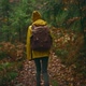 Slow Motion Camera Follows Woman Hiker in Yellow Raincoat and Knitted Beanie with Backpack Hiking in