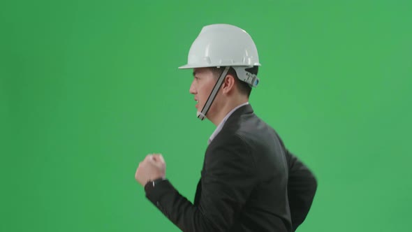 Side View Of Asian Chief Engineer In The Hard Hat Runs On Green Screen Chroma Key alt