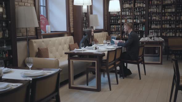 Brunette Woman and Blond Bearded Man Sitting at the Table in the Cafe Working alt