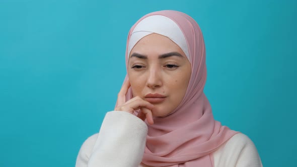 Thoughtful Young Muslim Woman in Hijab Rubbing Her Chin and Looking Aside with Pensive Expression