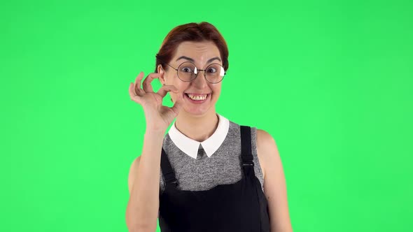 Portrait of Funny Girl in Round Glasses Is Making Sign Ok. Green Screen alt
