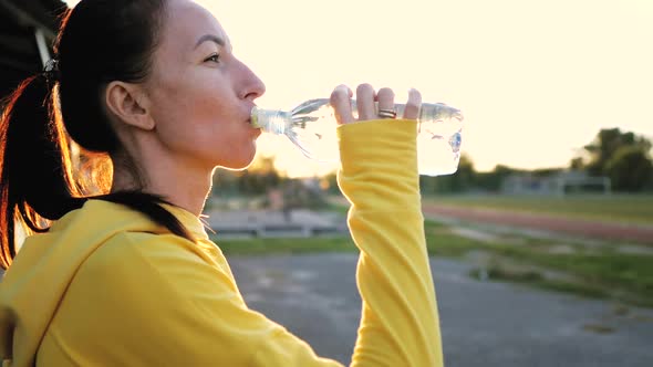 Fitness Young Woman Drinking From Sport Bottle During a Workout Pause in Stadium alt