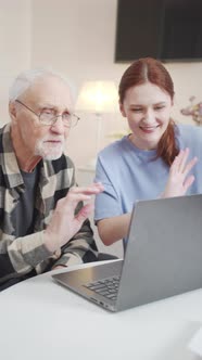 A Woman and an Elderly Man Sit in Front of a Laptop and Greet Interlocutors By Video Communication alt
