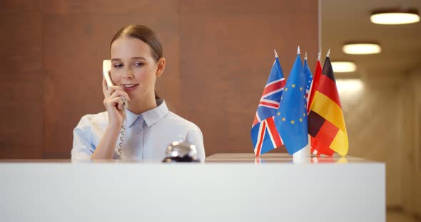 Smiling Young Businesswoman Talking on Telephone at Reception alt