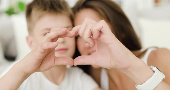 Smiling Young Mother and Her Teen Son Showing Heart Shape with Their Fingers