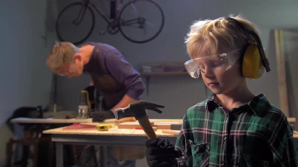 Boy in Glasses Stands and Looks at the Hammer  alt