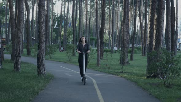 Girl rides electric scooter or e-scooter in city park at sunset. Eco e-mobility in urban city.  alt