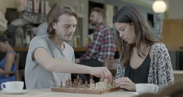 Man and woman talking and playing chess while sitting in pub