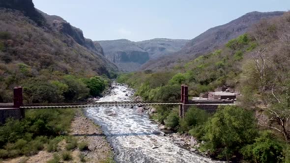 Aerial drone flying over a suspension bridge along a river in the Barranca de Huentitan National Par alt