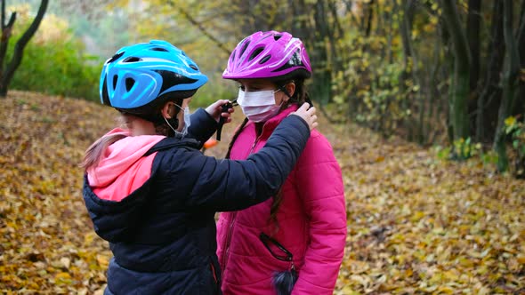 The Girl Helps Her Sister Put on a Safety Helmet Before Riding a Bicycle on a Sunny Autumn Day in
