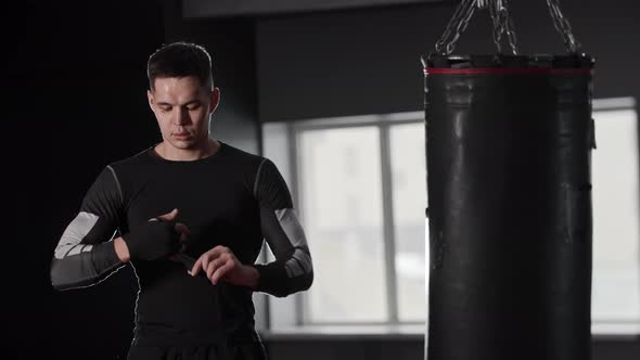 Athletic Young Man Boxer Bandaging His Hands Standing Near the Punching Bag alt