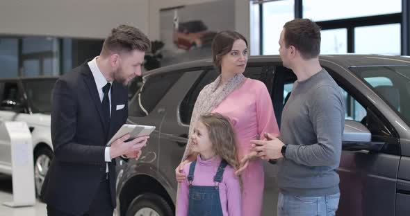 Confident Caucasian Car Dealer Presenting New Automobile To Young Family alt