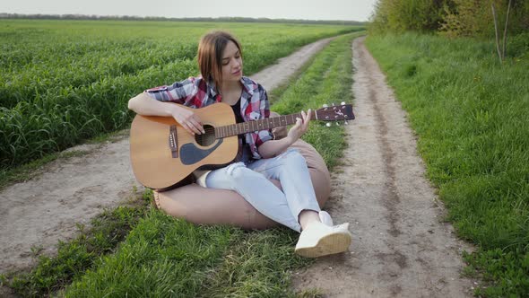 Woman Plays Music on Guitar and Sings on the Country Road Near Wheat Field alt