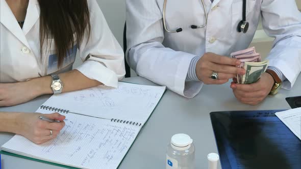 Male Doctor Counting Money and Giving It To His Female Colleague alt
