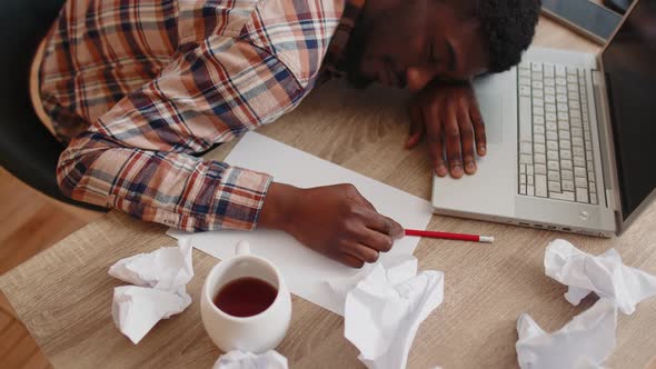 Tired Man at Home Office Falling Asleep on Table with Laptop Computer Crumpled Sheets of Paper alt