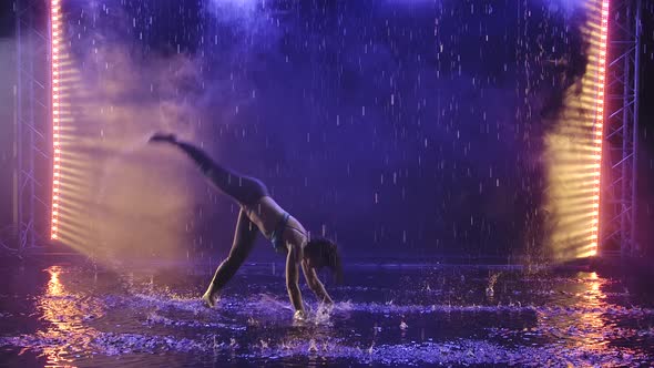 A Silhouette of a Sporty Woman Showing the Technique of Capoeira Martial Art in the Rays of Blue alt