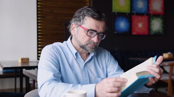 Mature Male Reads Book While Sitting in a Cafe alt