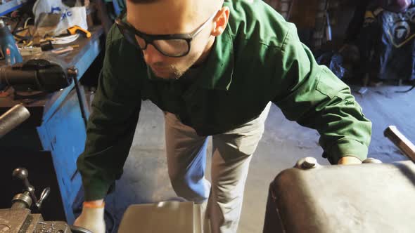 Male Mechanic in Protective Eyewear Uses a Turning Lathe to Processing Metal in Garage alt