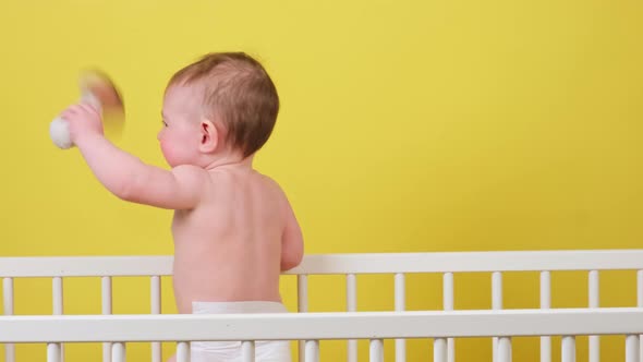 Happy infant baby boy is standing in a crib, yellow studio background. Smiling caucasian toddler kid