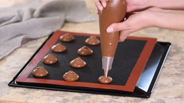 Cooking chocolate profiteroles, female hands squeeze the dough from the bag onto baking sheet alt