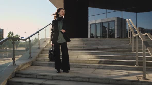 A Businesswoman Stands on the Stairs of a Large Corporation Looking Around