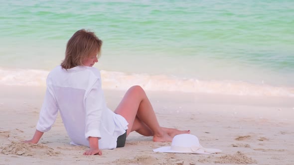 Young Woman Sitting on the Sand of the Empty Beach and Enjoy Weekend Vaccation