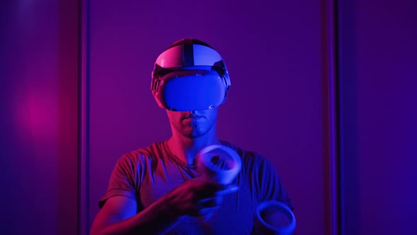Young Man in VR Helmet Interacts with Virtual Reality Using Controllers alt