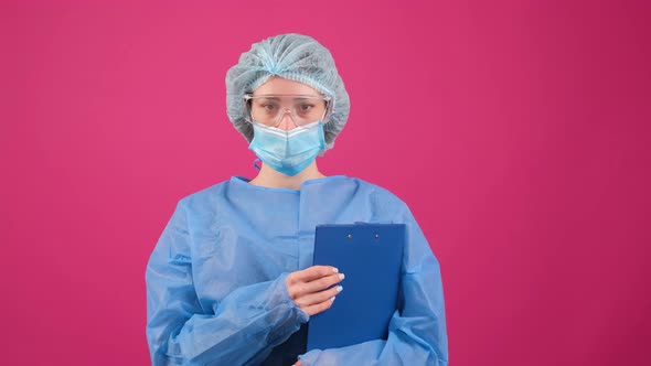Serious Doctor in a Blue Medical Coat Safety Glasses and Medical Cap Looking at Camera alt