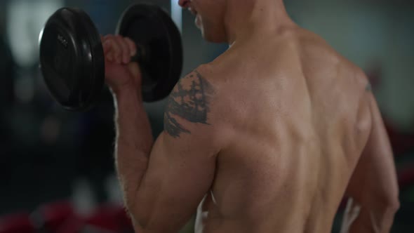 Unrecognizable Tattooed Sportsman Lifting Dumbbells Working Out in Gym Indoors alt