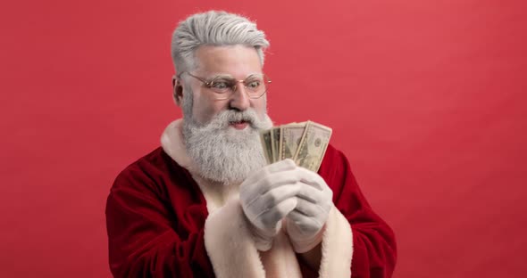 Funny Stylish Santa Claus on a Red Background Holds Money Dollars in His Hands