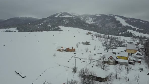 Flight Over a Village in Carpathian Mountains. Bird's Eye View of Snow-covered Houses in Mountains alt