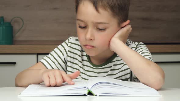 Portrait of a boy enthusiastically reading a book sitting at a table at home schooling. alt