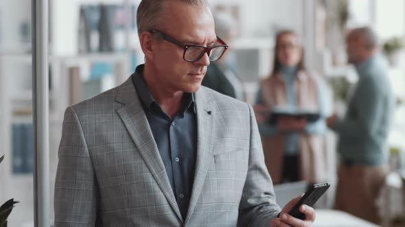 Joyous Businessman Using Smartphone and Posing for Camera in Office alt