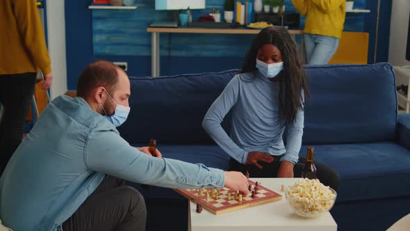 African Woman Wearing Face Mask Playing Chess with Man alt