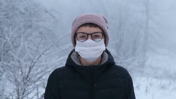 Young Woman in Surgical Mask with Glasses in Winter Background with Snowflakes Surround