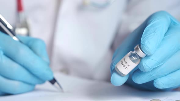 Hand in Latex Gloves Holding Glass Ampoule Vaccine and Writing on Paper alt