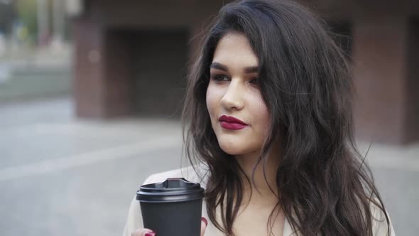 Beautiful Brunette with Red Lips Holds a Glass of Drink and Smiles at the Camera alt