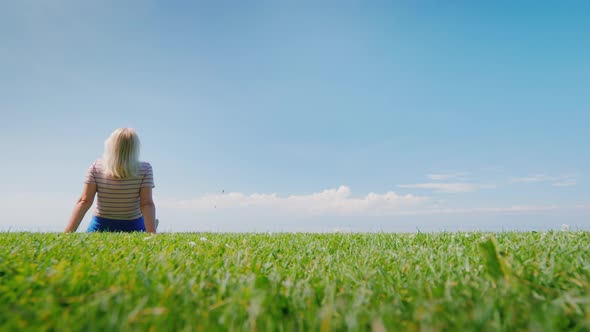 Woman Relaxes in Nature Sitting in a Picturesque Place on a Green Meadow alt