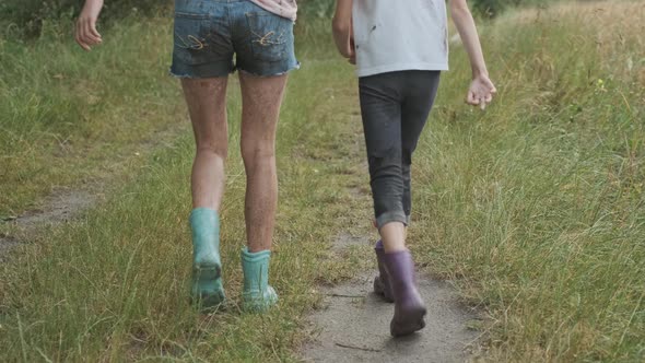 Two Happy Girls Sisters Walking After the Rain in Dirty Clothes Holding Hands Back View alt