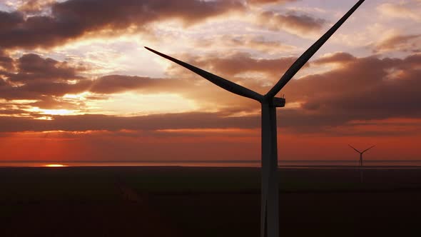 Wind Farm with Large Propellers Rotating at Sunset in Field