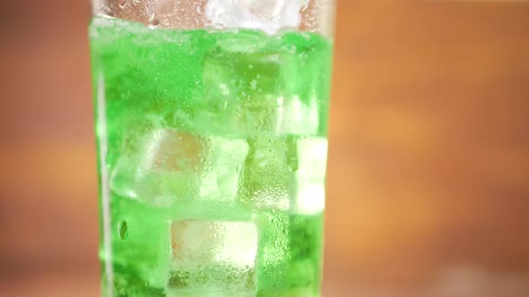 Green Soda Pouring Into Glass with Ice Cube