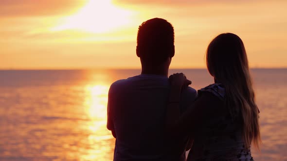 Multi-ethnic Couple in Love Admires the Sunset Over the Ocean alt