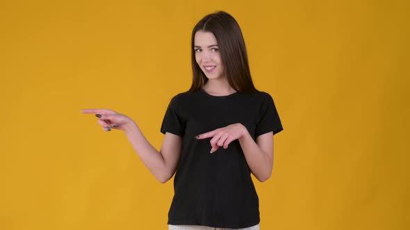 Young cheerful girl with long hair in a black T-shirt pointing empty place