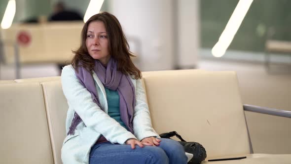 Annoyed Female Passenger Is Sitting in Terminal of Airport, Delay or Canceled Flight, Portrait alt