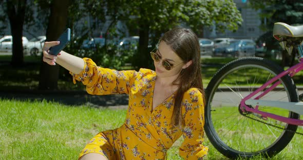 Attractive Girl Taking a Selfie on Smart Phone Sitting in the Park on the Grass. Close-up Beautiful alt