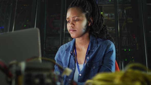 African american female computer technician using laptop working in business server room alt