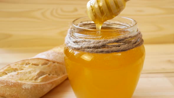 A Wooden Spoon Scoops Up Liquid Honey From a Glass Jar