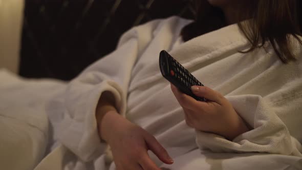 A Woman Lies Rests Switches the Remote Control Channels on the TV in a Hotel