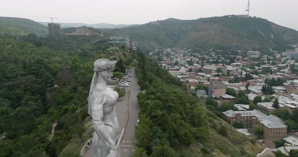Arc aerial shot of the Kartlis Deda statue and Tbilisi during an overcast day. alt
