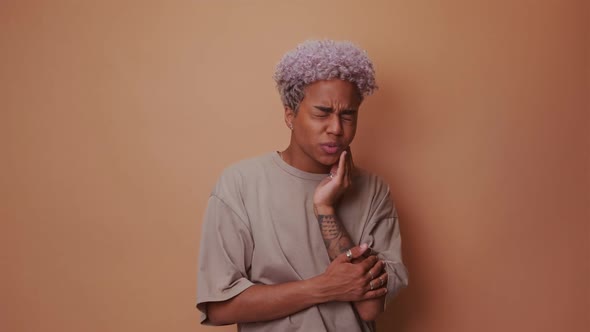 Dark Skinned Woman Suffers From Toothache Touches Cheek on Beige Background alt